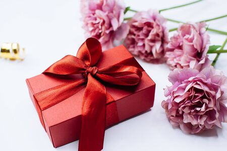 White background with red gift box and peony flowers, top view. Flat lay style