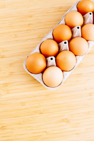 Overhead view of fresh brown chicken eggs in open egg carton box on wooden table background. Top view with copy space. Natural healthy food and organic farming concept.の写真素材