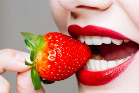 Macro close up of caucasus woman's lips with red lipstick and fresh strawberry. Food pleasure, healthy food conceptの写真素材