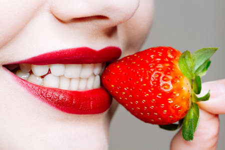 Macro close up of caucasus woman's lips with red lipstick and fresh strawberry. Food pleasure, healthy food conceptの写真素材