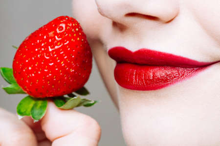 Macro close up of caucasus woman's lips with red lipstick and fresh strawberry. Food pleasure, healthy food conceptの写真素材