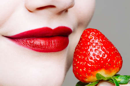 Macro close up of caucasus woman's lips with red lipstick and fresh strawberry. Food pleasure, healthy food conceptの写真素材