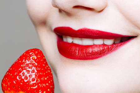 Macro close up of caucasus woman's lips with red lipstick and fresh strawberry. Food pleasure, healthy food conceptの写真素材