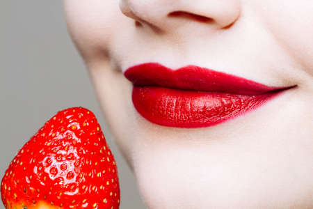 Macro close up of caucasus woman's lips with red lipstick and fresh strawberry. Food pleasure, healthy food conceptの写真素材
