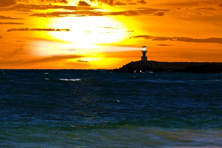 Lighthouse with light beam and turquoise sea at sunsetの写真素材