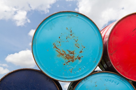Stack of different color 200 litre metal oil or chemical barrels in storage areaの写真素材