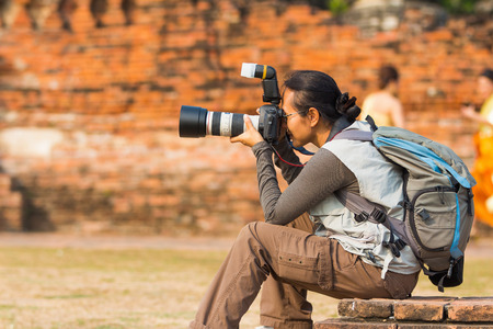 Tourist woman with backpack takes photo in Thai old templeの写真素材