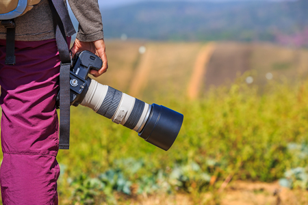 Photographer holds her DSLR camera with telephoto lens in her right handの写真素材