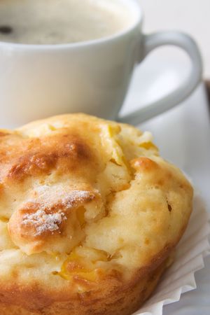 Selective focus image of a mango muffin with a cup of espresso on a white plate