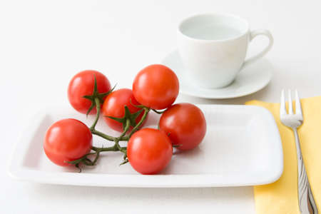 Tomatoes and water served with white dishes like cake and coffee as symbol for loosing weight with pleasure.の写真素材