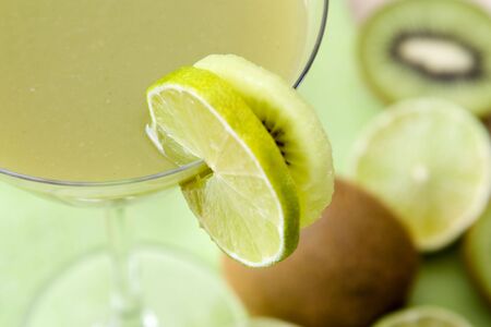 Close-up image of a glass with a green fruit juice and lime and kiwi fruits as decoration.の写真素材