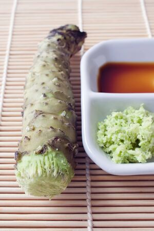 Selective focus image of a fresh wasabi root also called Japanese horseradish with soy sauce on a bamboo mat.の写真素材