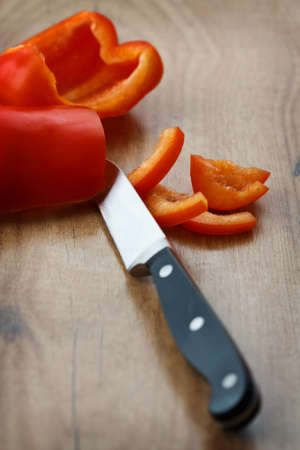 Cut red bell pepper with a kitchen knife on a wooden board.の写真素材