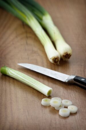 Close up image of spring onions which are cut and a kitchen knife on a wooden board.の写真素材