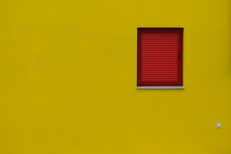 Close-up image of a yellow wall with a red window and a socket.の写真素材