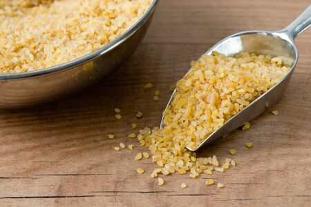 Bowl with uncooked bulgur and a chute on a wooden board.の写真素材