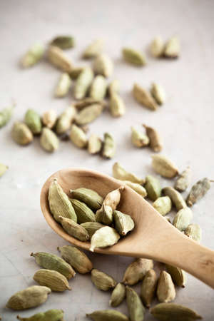 Green cardamom seeds and a wooden spoon on stone.の写真素材