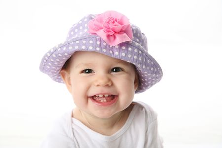 Smiling baby girl showing teeth wearing a purple polka dot hat with pink flower isolated on white backgroundの写真素材