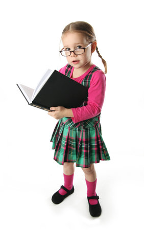 Cute preschool age girl wearing eyeglasses carrying a stack of heavy booksの写真素材