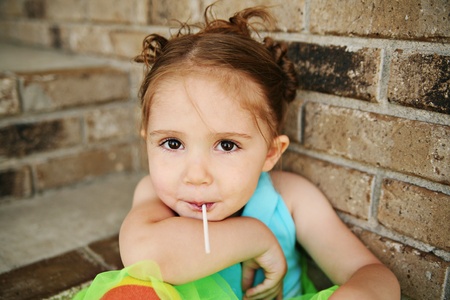 Portrait of a young girl sitting on brick steps eating a lollipop, wearing rainbow tights and a bright green tutuの写真素材