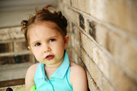 Portrait of a young girl sitting on brick steps eating a lollipop, wearing rainbow tights and a bright green tutuの写真素材