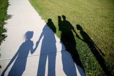 Shadows of a family of five walking in the park holding handsの写真素材