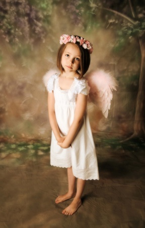 Beautiful young girl wearing angel wings and flower halo with somber expressionの写真素材