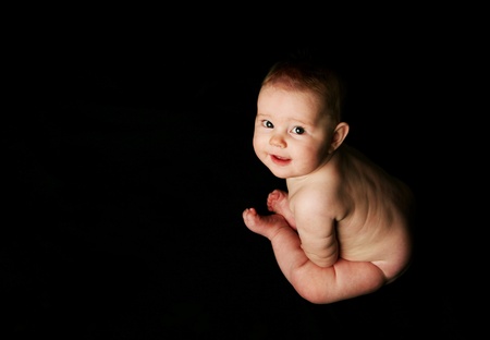 Baby sitting up facing sideways nude on black backgroundの写真素材