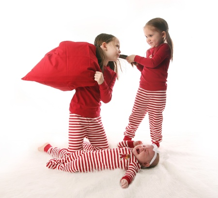 Three sisters dressed in Christmas pajamas. Two older girls are pulling hair and having a pillow fight while the baby is crying.の写真素材