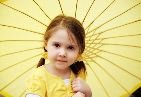Cute little girl with pigtails holding a yellow parasol outsideの写真素材