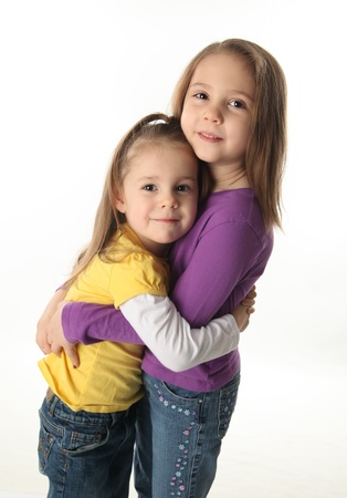 Two cute young sisters standing up hugging each other, isolated on whiteの写真素材