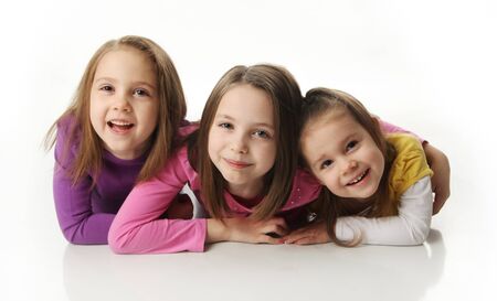 Three cute young sisters hugging each other, isolated on whiteの写真素材
