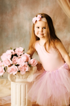 Adorable little girl dressed as a ballerina in a tutu standing next to pink roses.の写真素材
