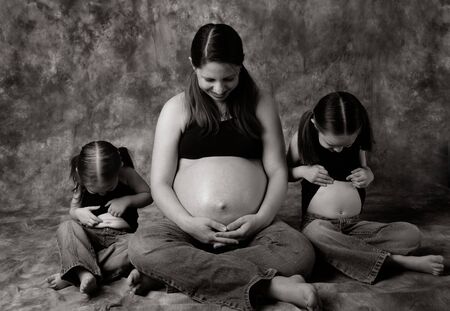 Maternity portrait of a pregnant mom and her two daughters all looking at their belliesの写真素材
