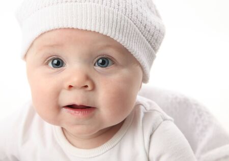 Closeup portrait of an adorable smiling baby wearing a white knit hatの写真素材