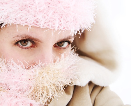Portrait of pretty woman with face covered by scarf and hat outside in the snow