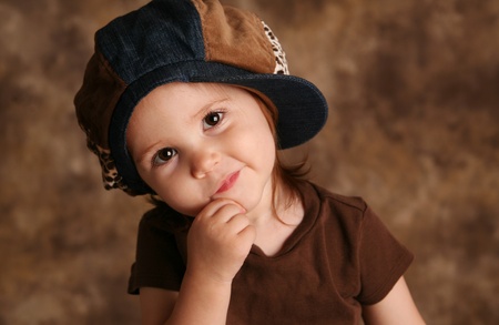 Portrait of an adorable toddler girl modeling a brown and blue jean denim hat posing for the cameraの写真素材