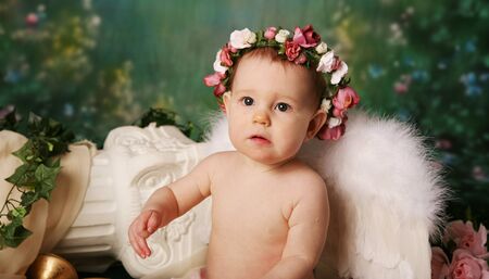 Beautiful young girl wearing angel wings and flower halo with somber expressionの写真素材
