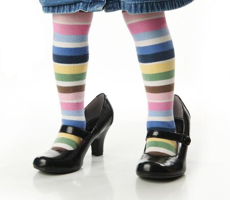 Toddler girl wearing bright colored striped tights trying on mother's high heel shoesの写真素材