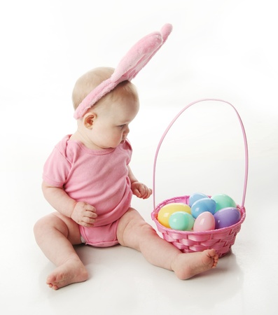 Portrait of a cute baby dressed in Easter bunny ears with a basket full of eggsの写真素材