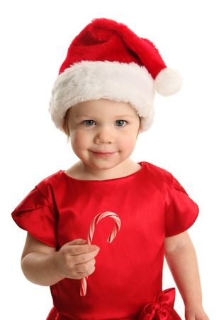 Christmas Portrait of a beautiful little child girl wearing a santa hat and holding a candy caneの写真素材