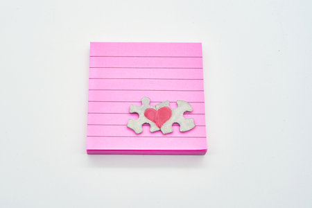 Heart on connected puzzle pieces on top of note pink note pad on solid white backgroundの写真素材
