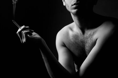photo of the lonely guy holding in hand a cigarette, against a dark background or the roomの写真素材