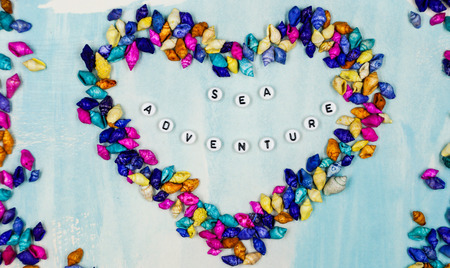 The phrase Sea adventure, has been placed inside the heart of small colorful shells on a blue...
