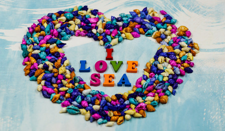 The phrase "I love sea", has been placed inside the heart of small colorful shells on a blue background.の写真素材