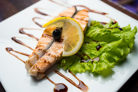 Barbecue fish steak on a white plate decorated with lemon and salad.の写真素材