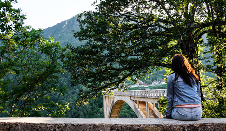 The girl in denim clothes sitting on the edge of the fence and looks at the bridge ?ur?evi?a.の写真素材