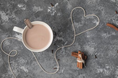 A white cup of hot cocoa drink with cinnamon sticks and white cotton yarn heart for Saint Valentines dayの写真素材