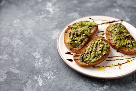 A freshly made minced avocado toast with balsamico dressing, linseed or flaxseed and oil on a white...