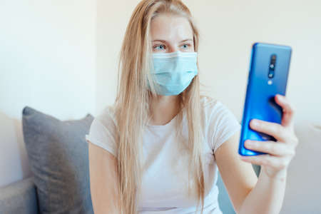 Blonde girl on a self-isolation having a video call with smartphoneの写真素材